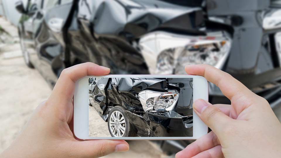 Unfallwagenankauf Mainz: Unfallschaden an einem Auto wird mit dem Smartphone fotografiert.